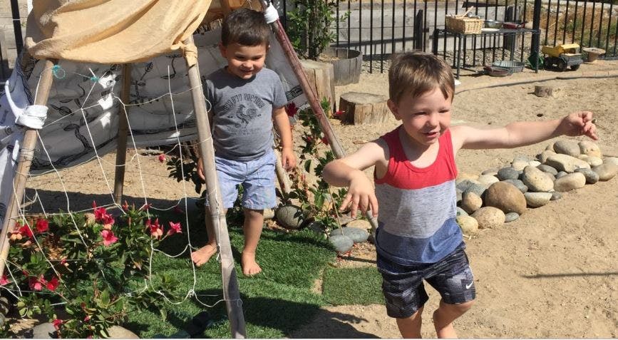 Two children playing outdoors near a tent-like structure outdoors