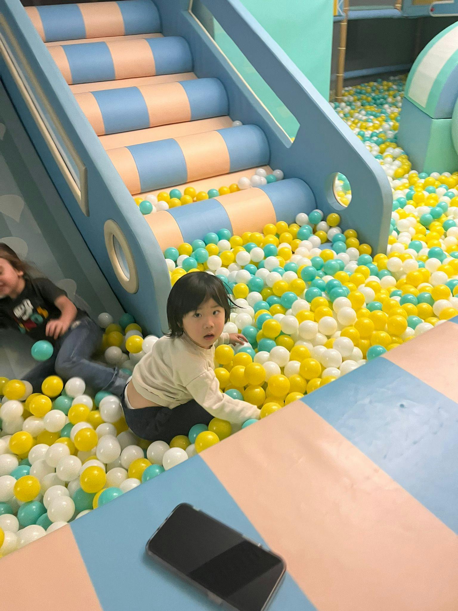 Two children playing in a ball pit with a slide