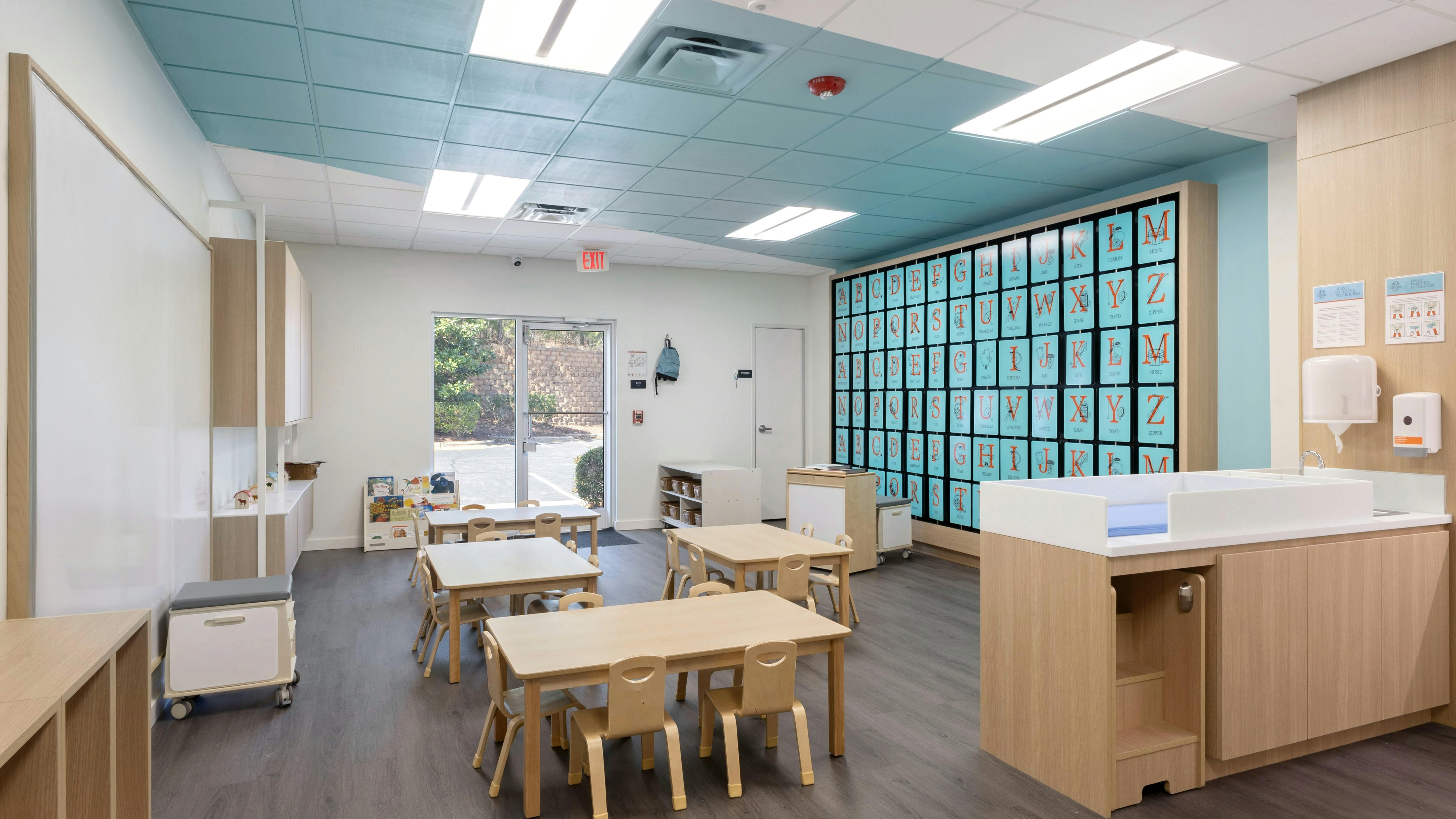 An empty childcare classroom with small tables and chairs, and a changing station