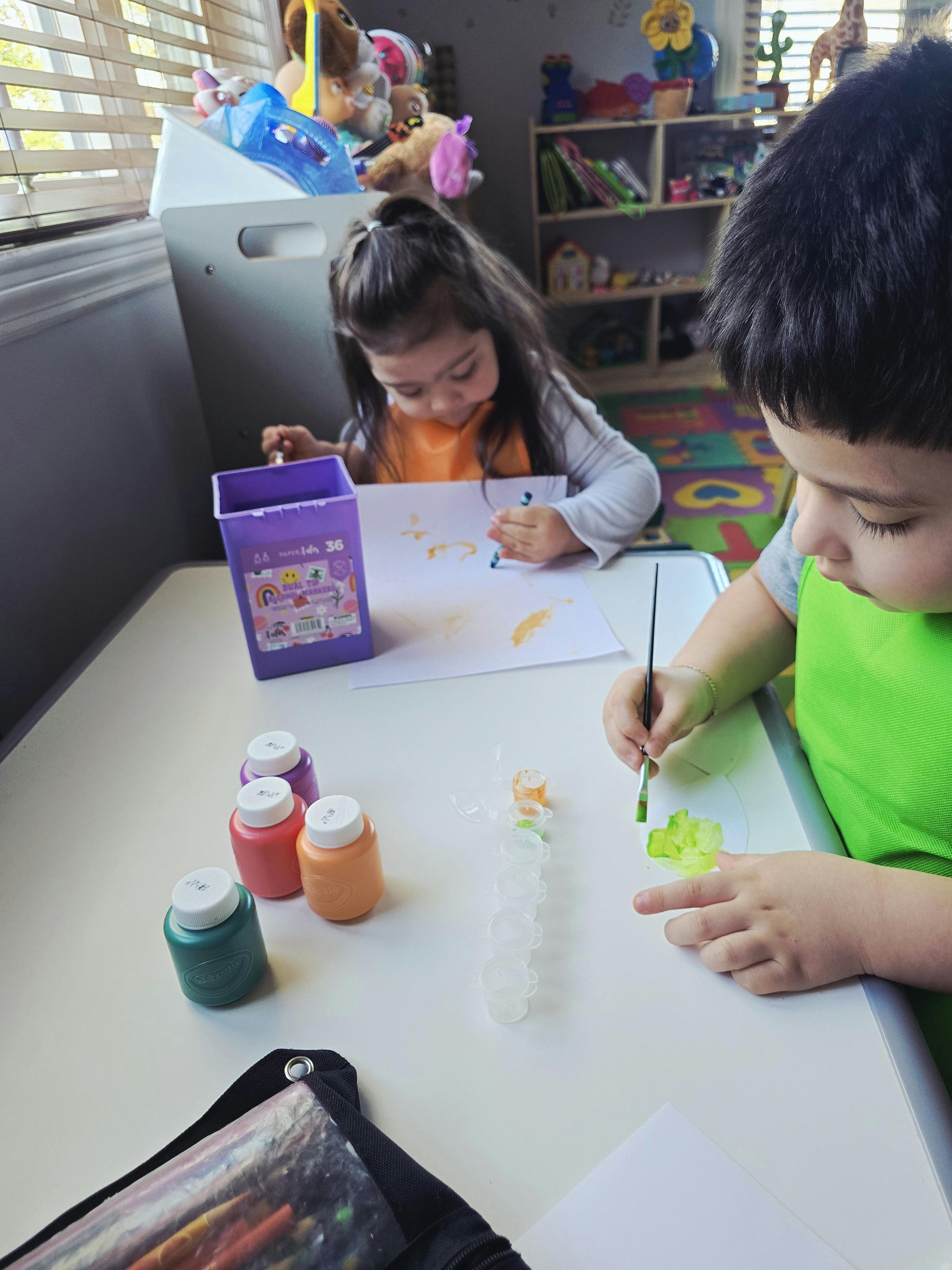 Two children painting and coloring at a table
