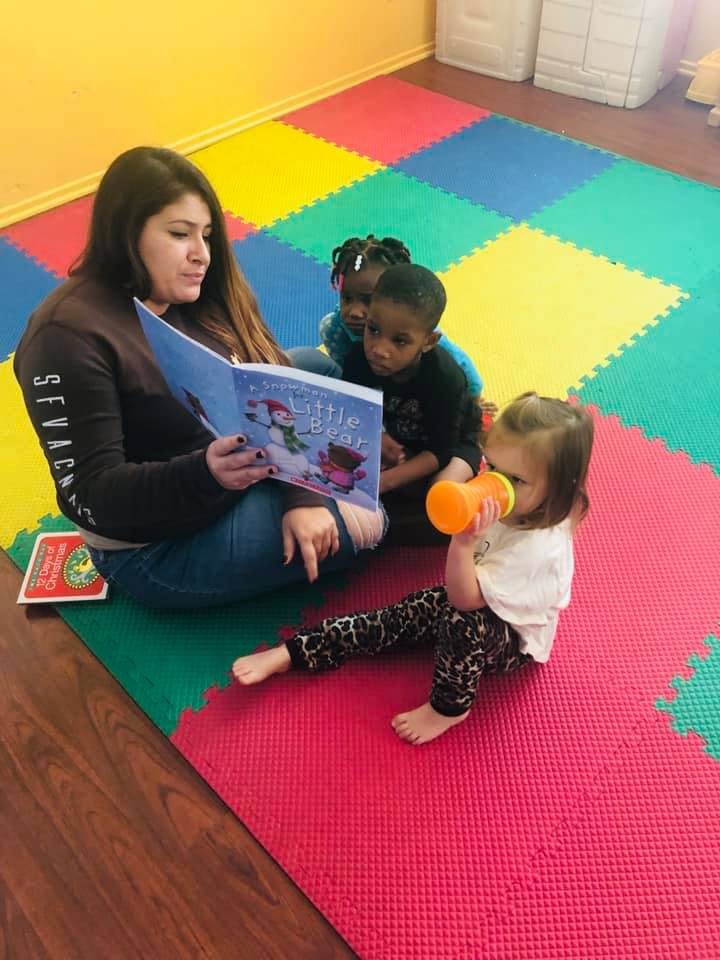 Person reading a book to three children on a colorful mat