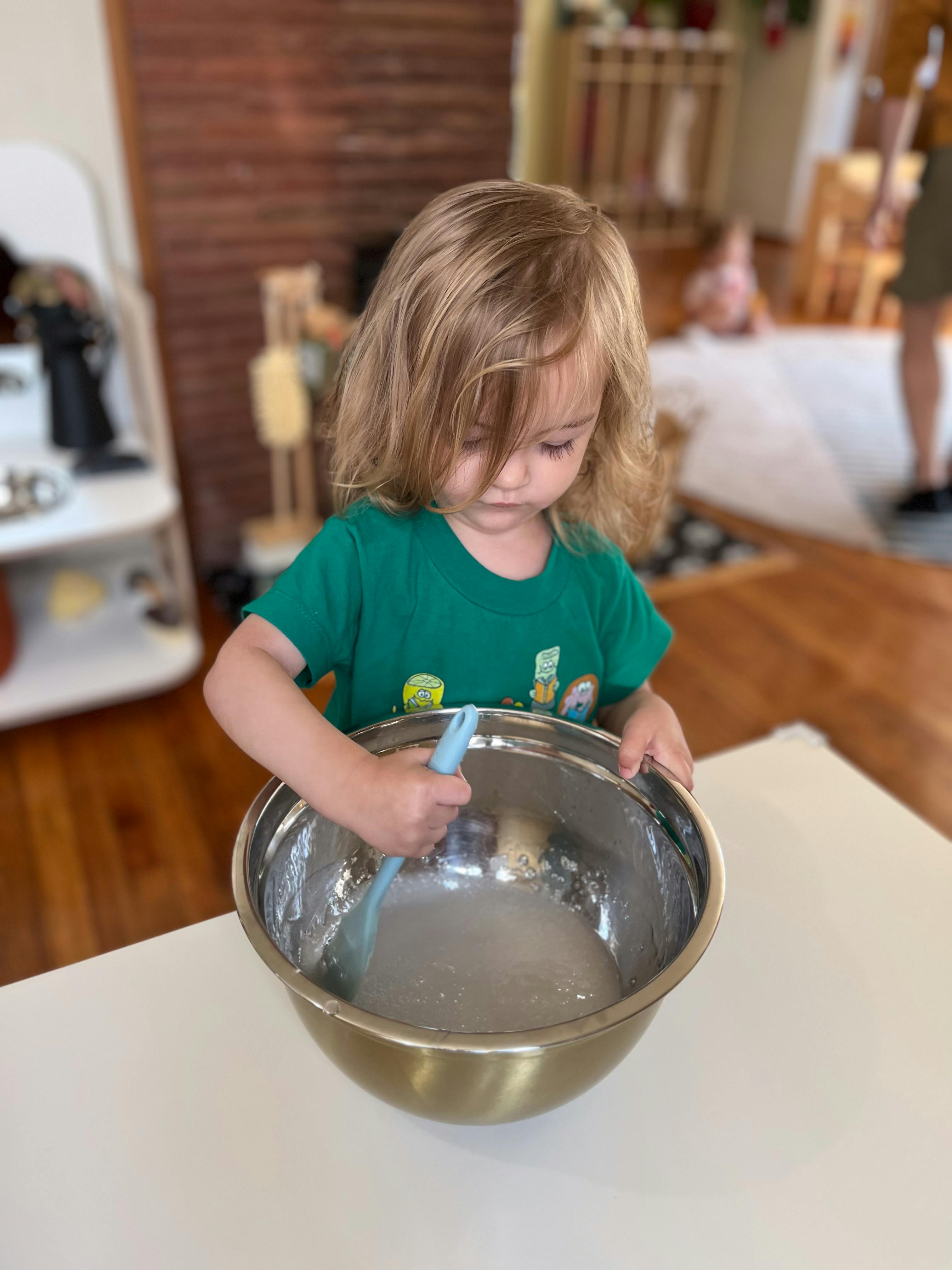Child stirring a mixture in a large metal bowl