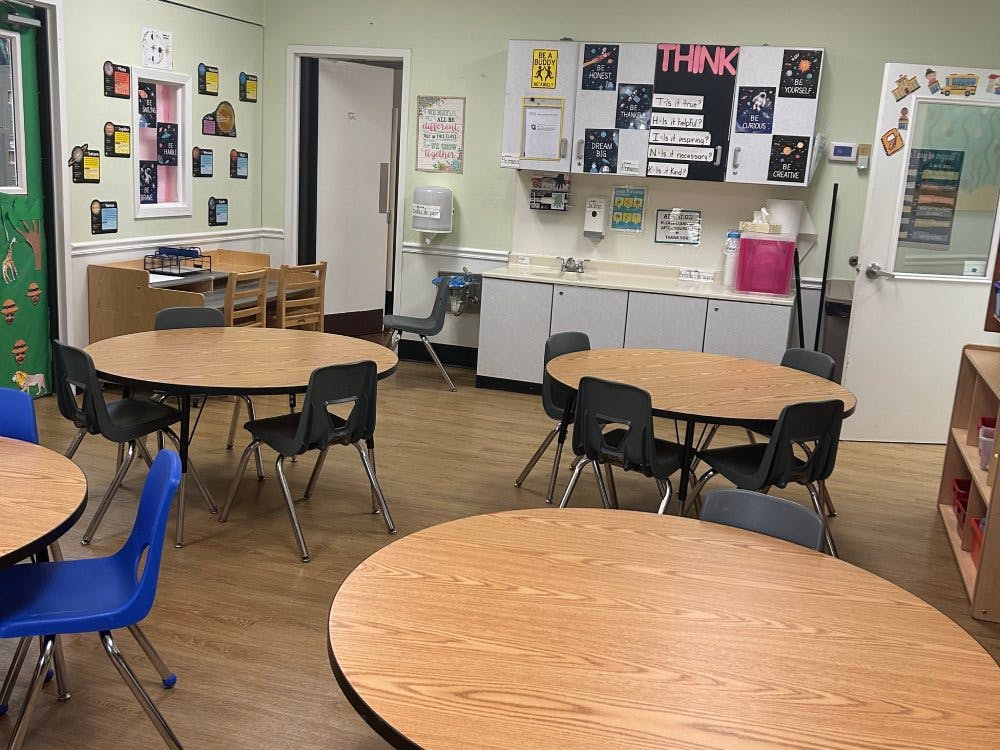 Classroom with multiple oval tables and chairs, and a counter with a sink