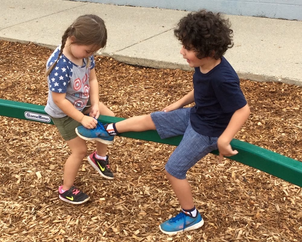 Child tying shoe of another child on a playground