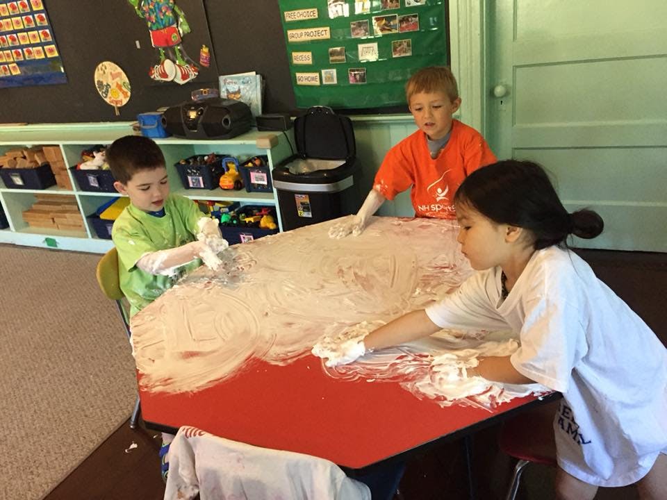 Three children playing with shaving cream on a red table