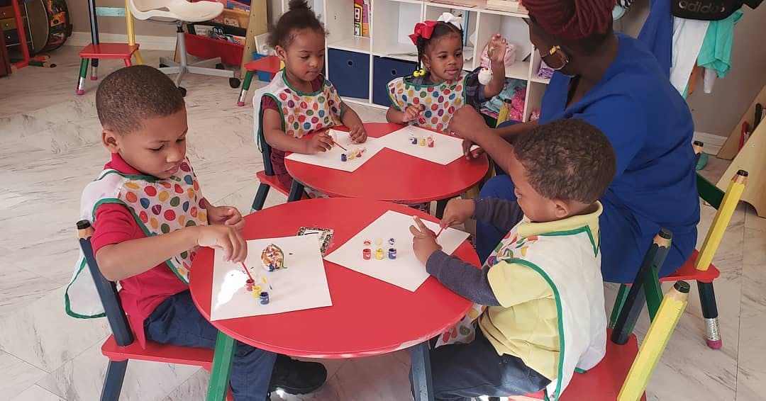 Adult and three children at small tables with papers and small objects