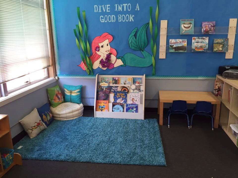 Children's reading nook with a blue rug, bookshelf, and mermaid wall decor