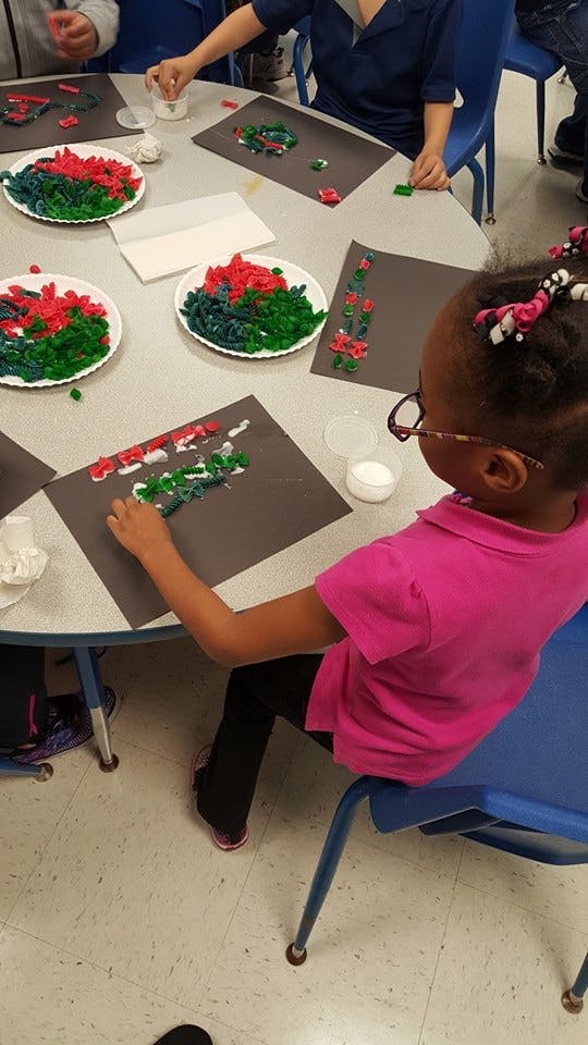 Child creating art with colored pasta on paper at a table