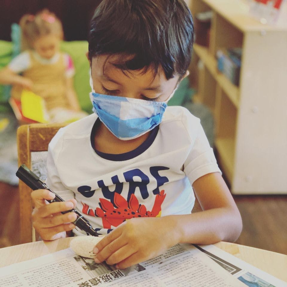 Child in a face mask holding a marker and a shell