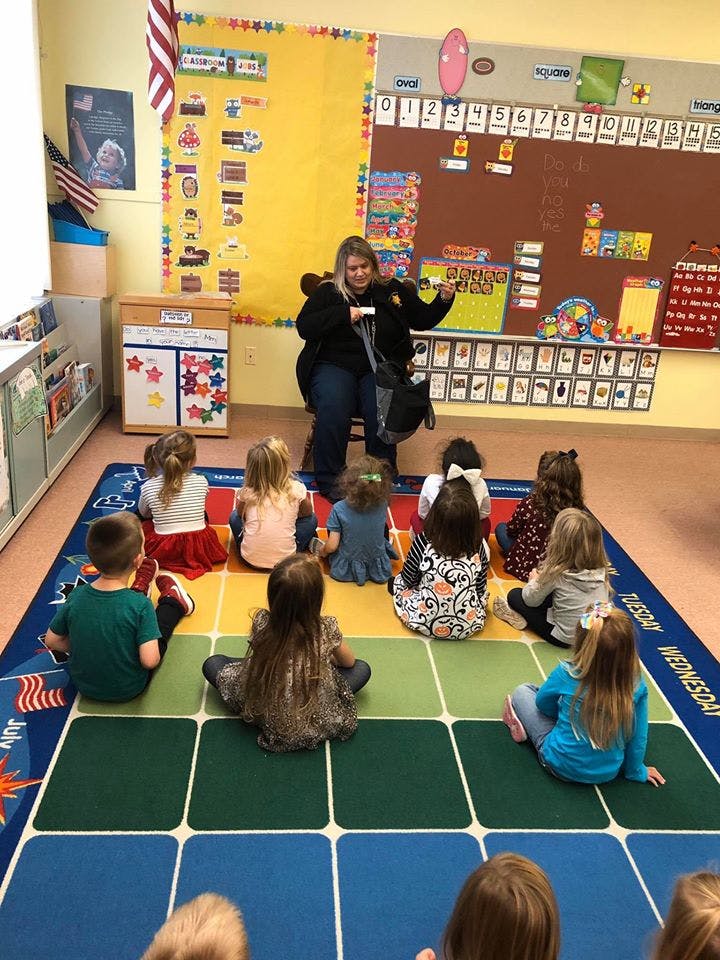 Adult speaking to a group of children sitting on a rug in a classroom