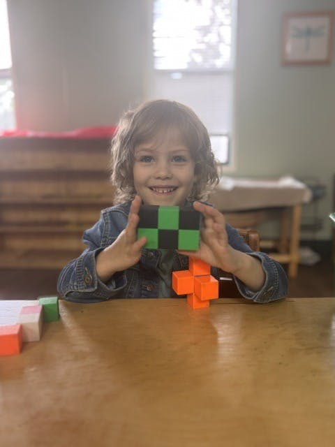 Child holding a small block structure at a table
