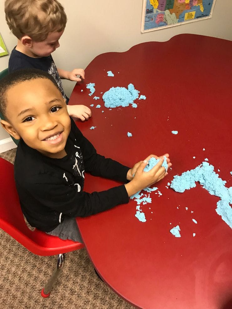 Two children playing with blue kinetic sand on a red table