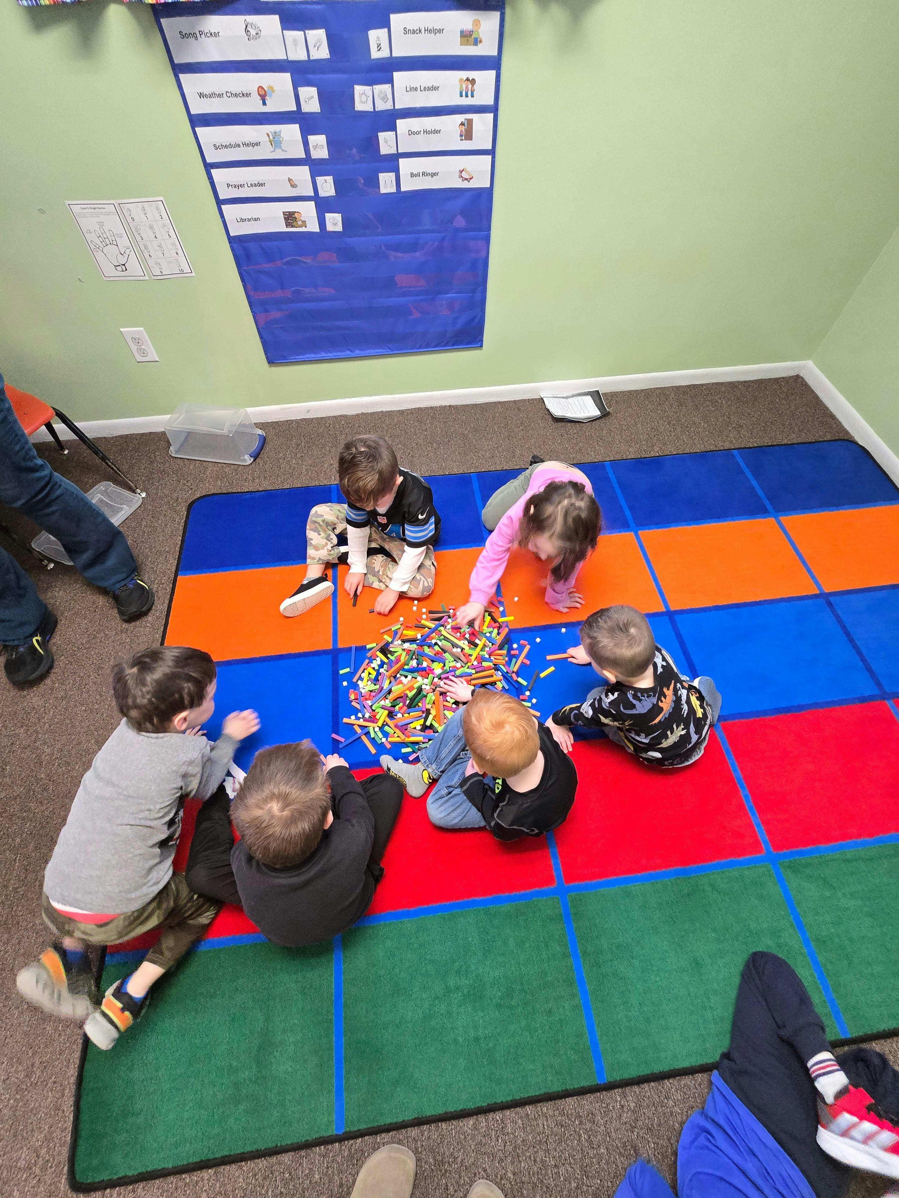 Several children sitting on a colorful mat playing with building sticks in a classroom