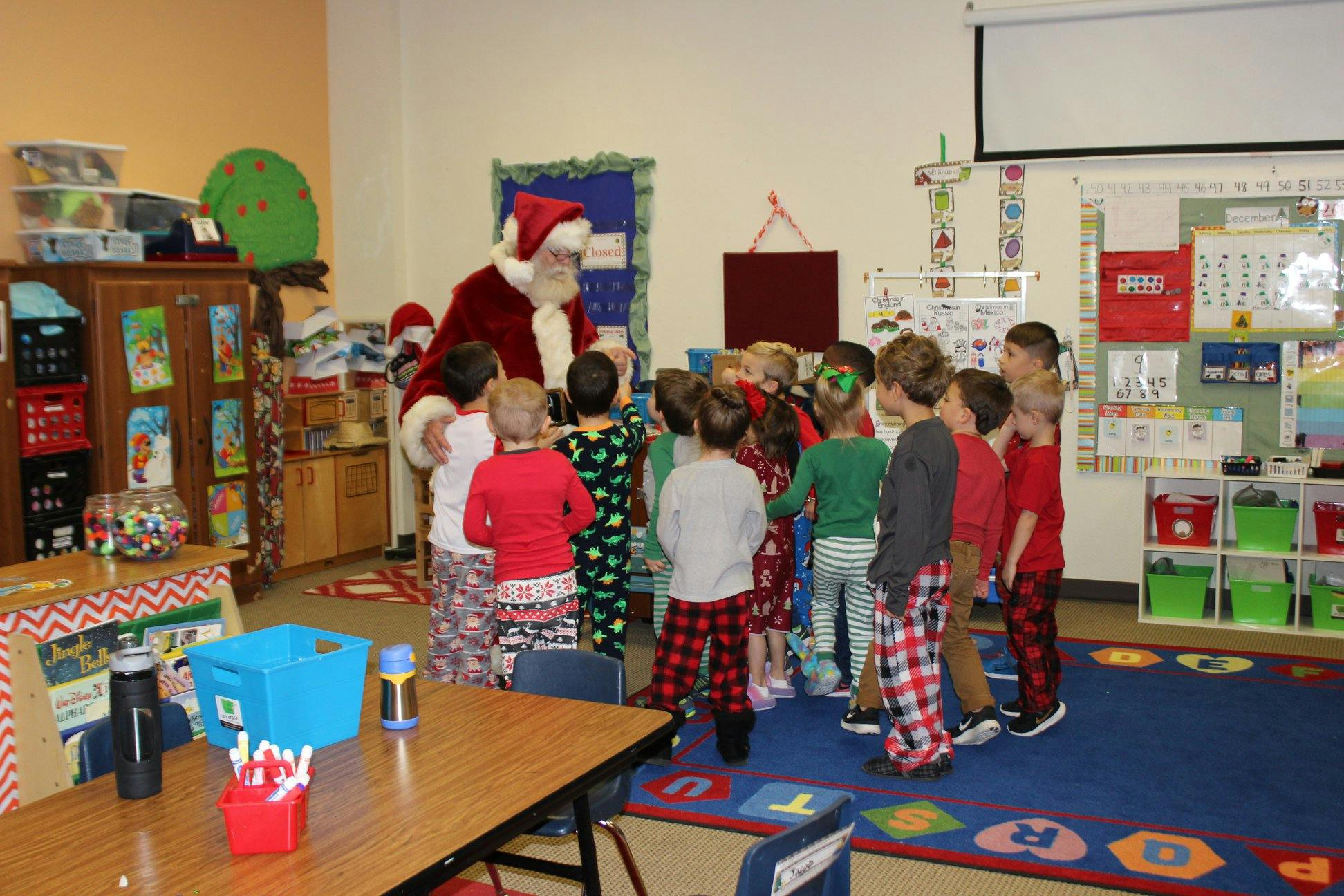 Person dressed as Santa Claus with a group of children in a classroom