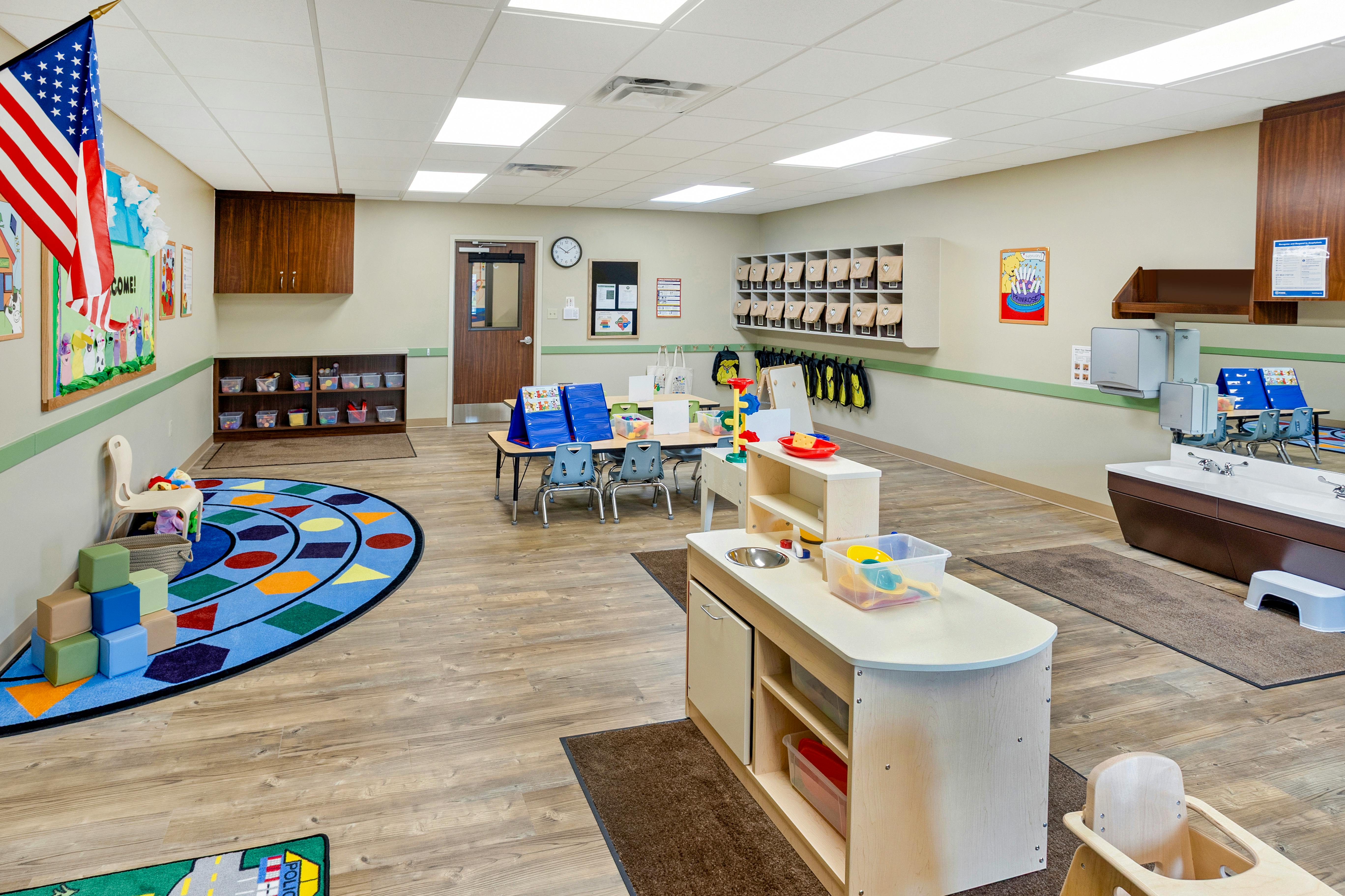 A colorful preschool classroom with play sinks, tables, and a geometric rug