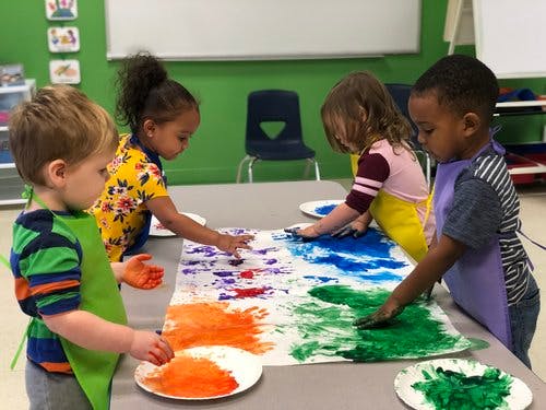 Four children finger painting on a large sheet of paper