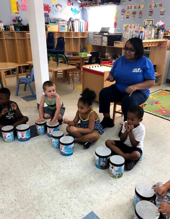 Adult and children sitting on floor with drums