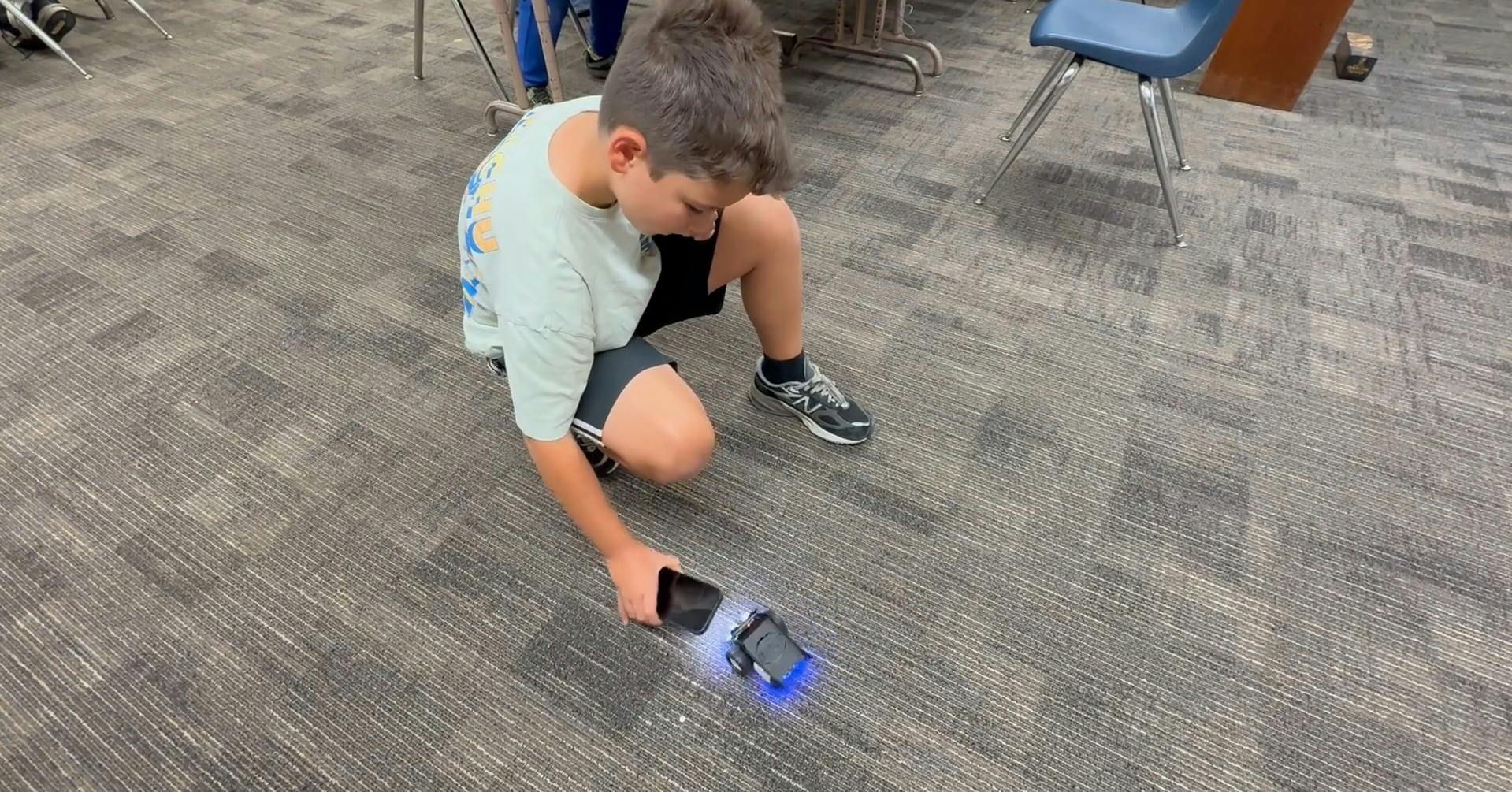 Child crouching on floor, holding phone over small glowing device