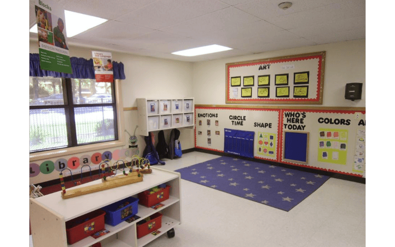 An empty preschool classroom with educational posters and a blue star rug