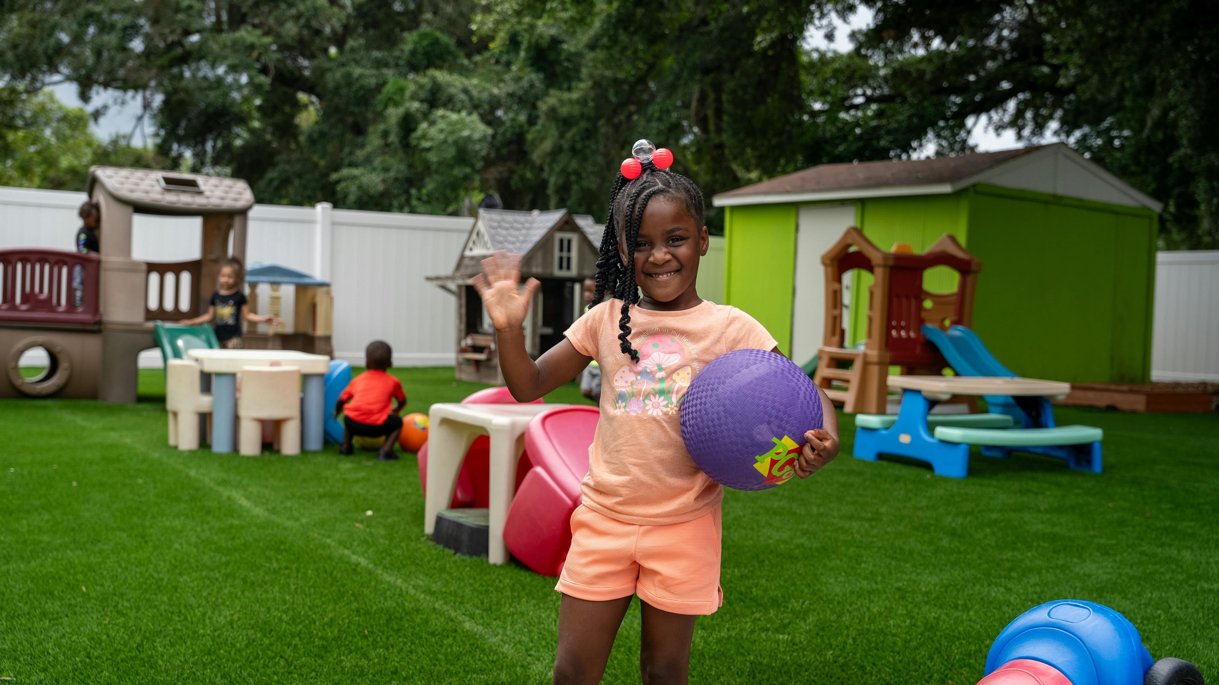 Child holding a ball and waving in a playground