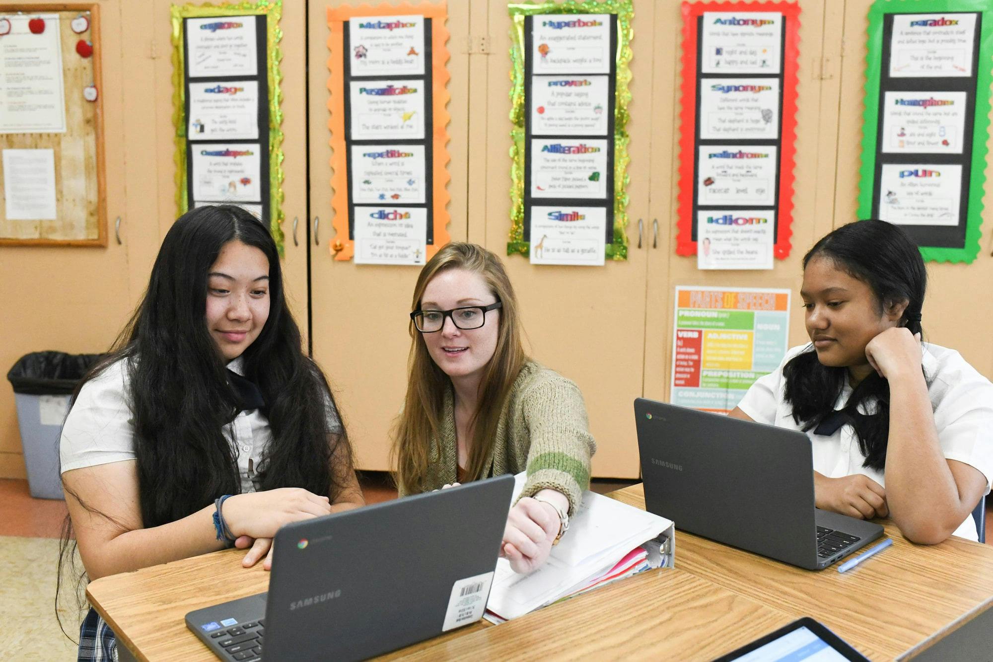 Three people sitting at desks with laptops in a classroom