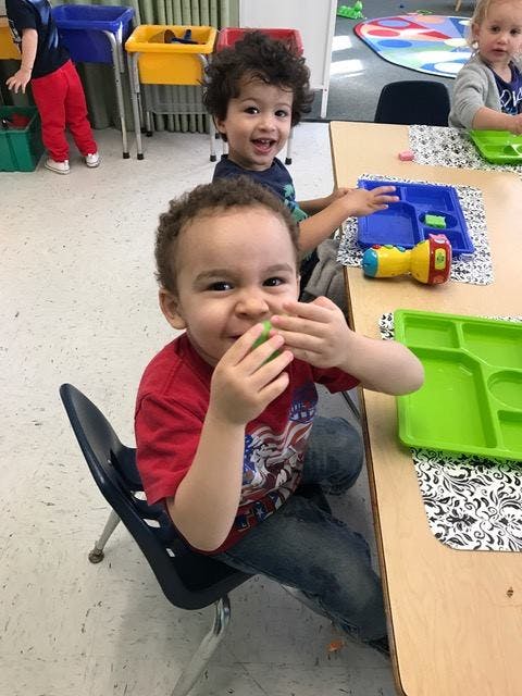 Child in red shirt holding a small green object, another child in background