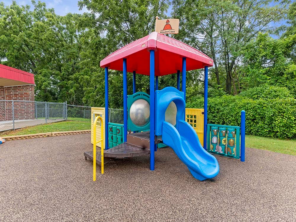 A colorful playground set with a red roof and blue slide on a playground surface