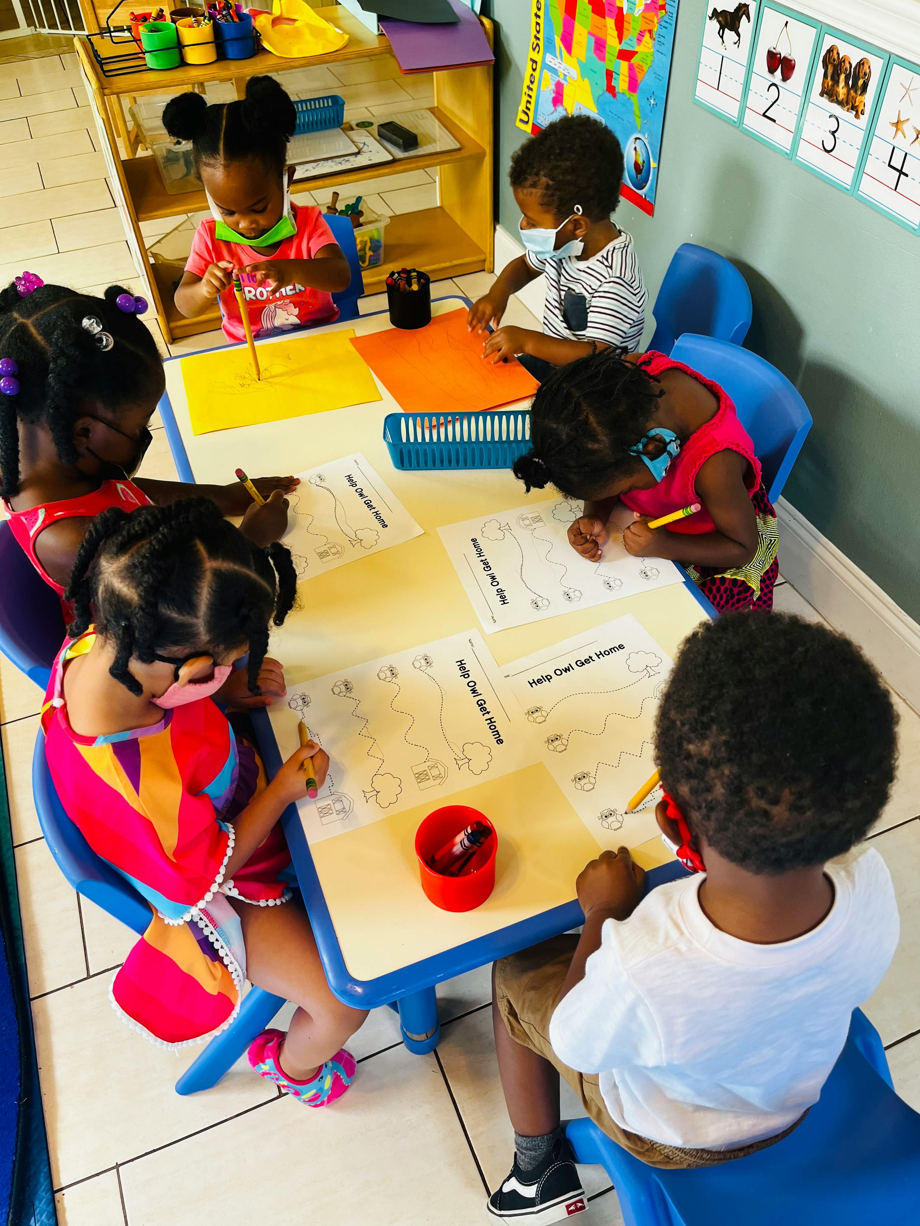 Children sitting at a table and drawing on papers in a classroom