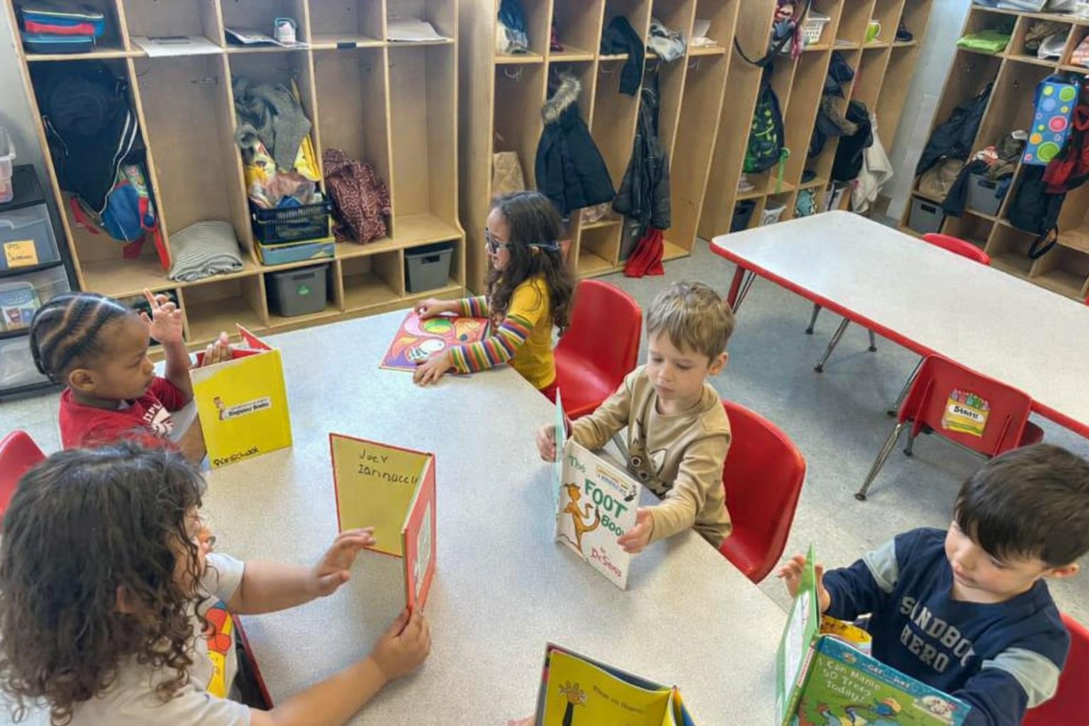 Four young children sitting at a table reading books in a classroom