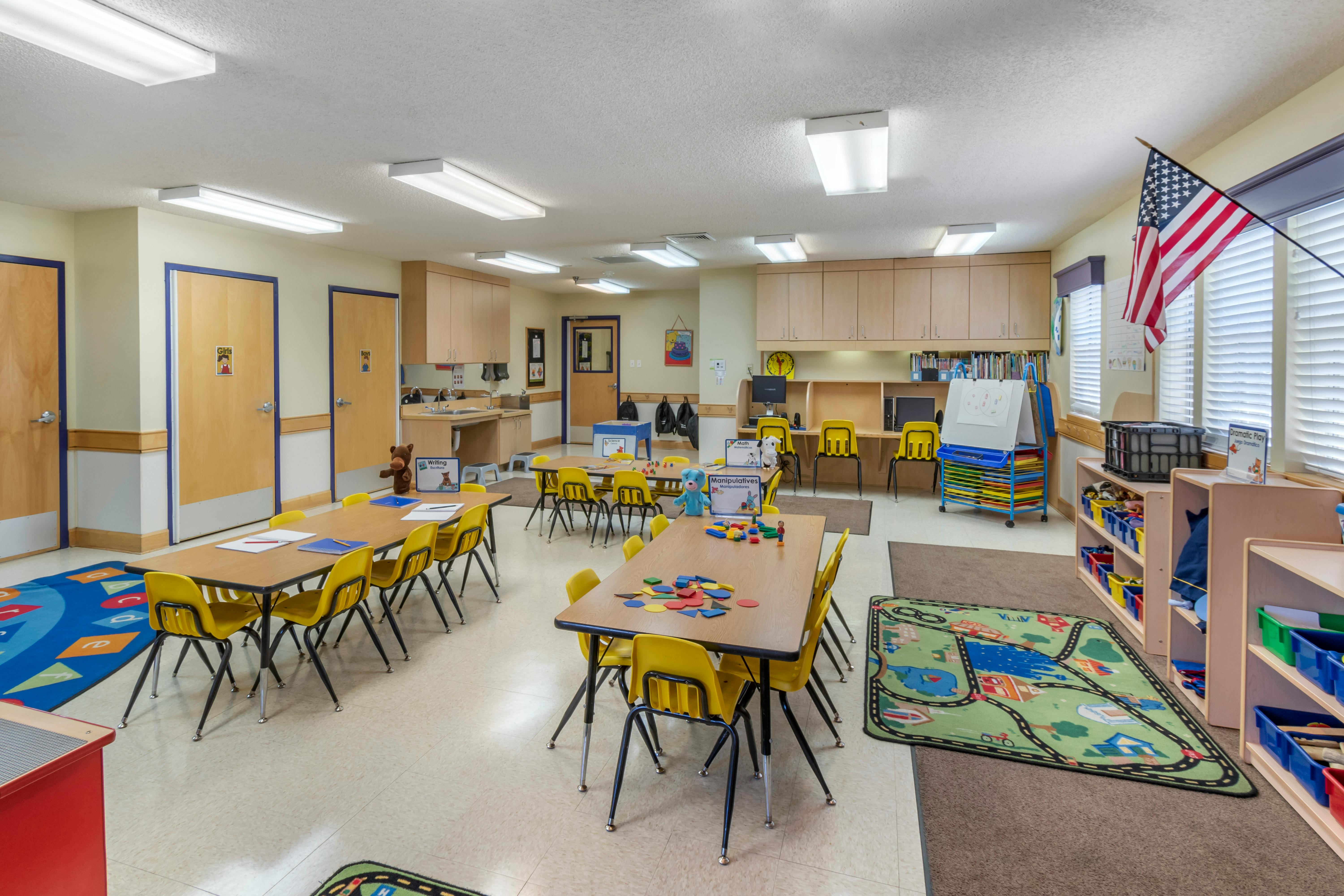 Classroom with tables, yellow chairs, and activity rugs