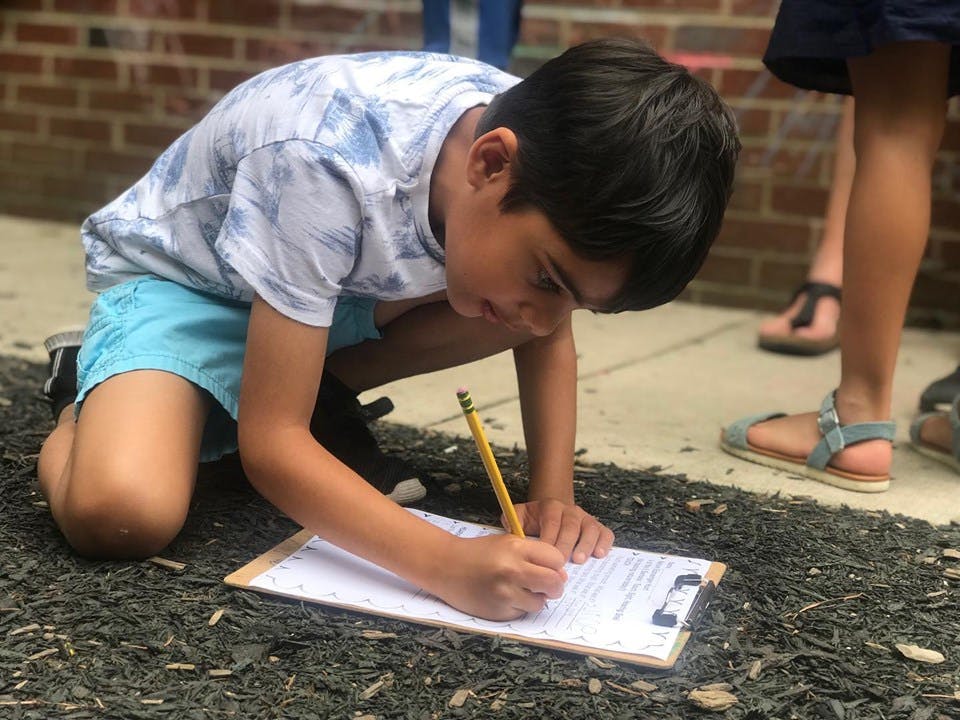 Child kneeling and writing on a clipboard with a pencil