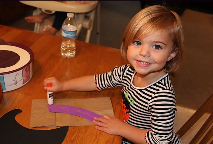 Child gluing purple paper onto cardboard