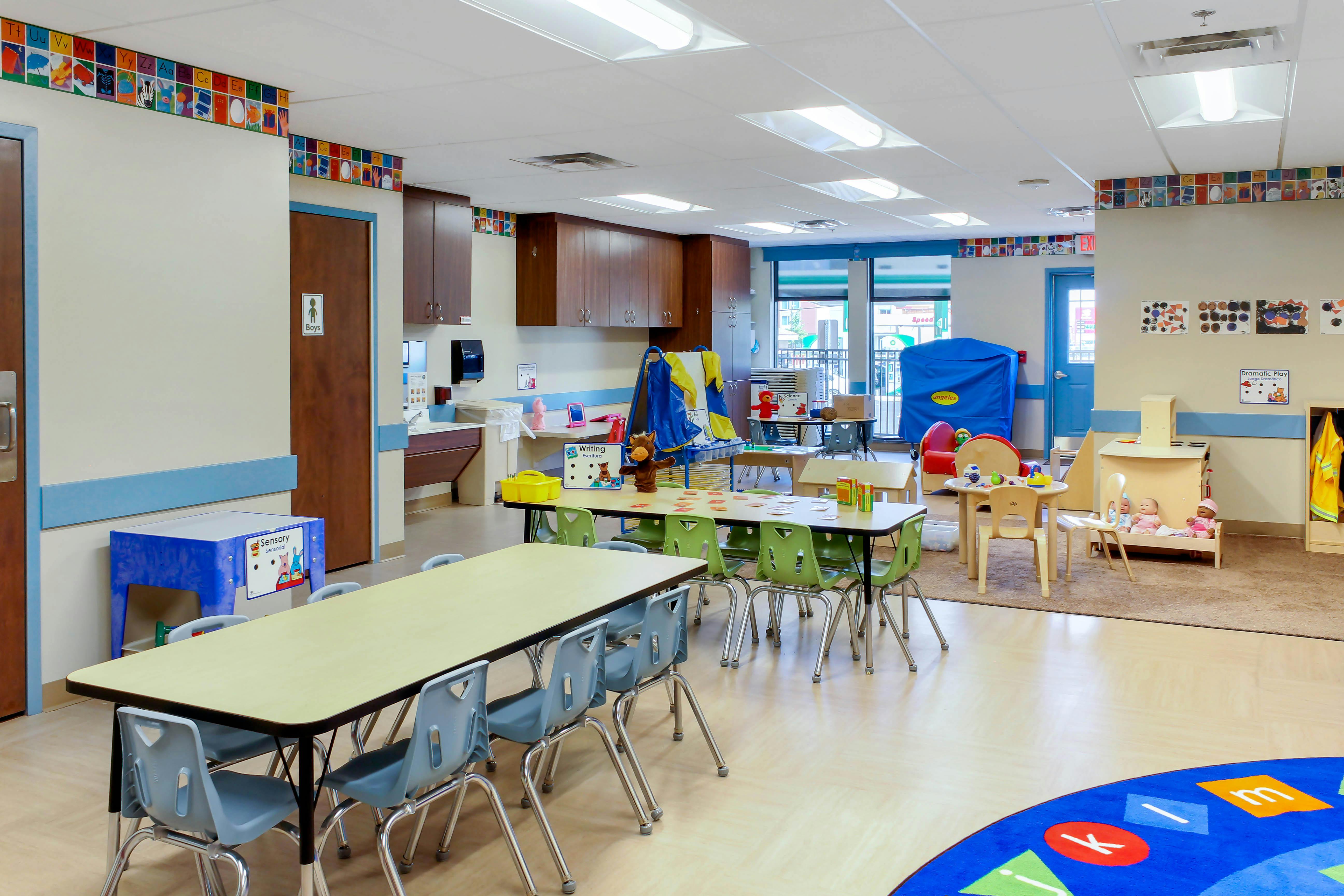 An empty early childhood classroom with multiple tables and chairs, toys, and learning centers