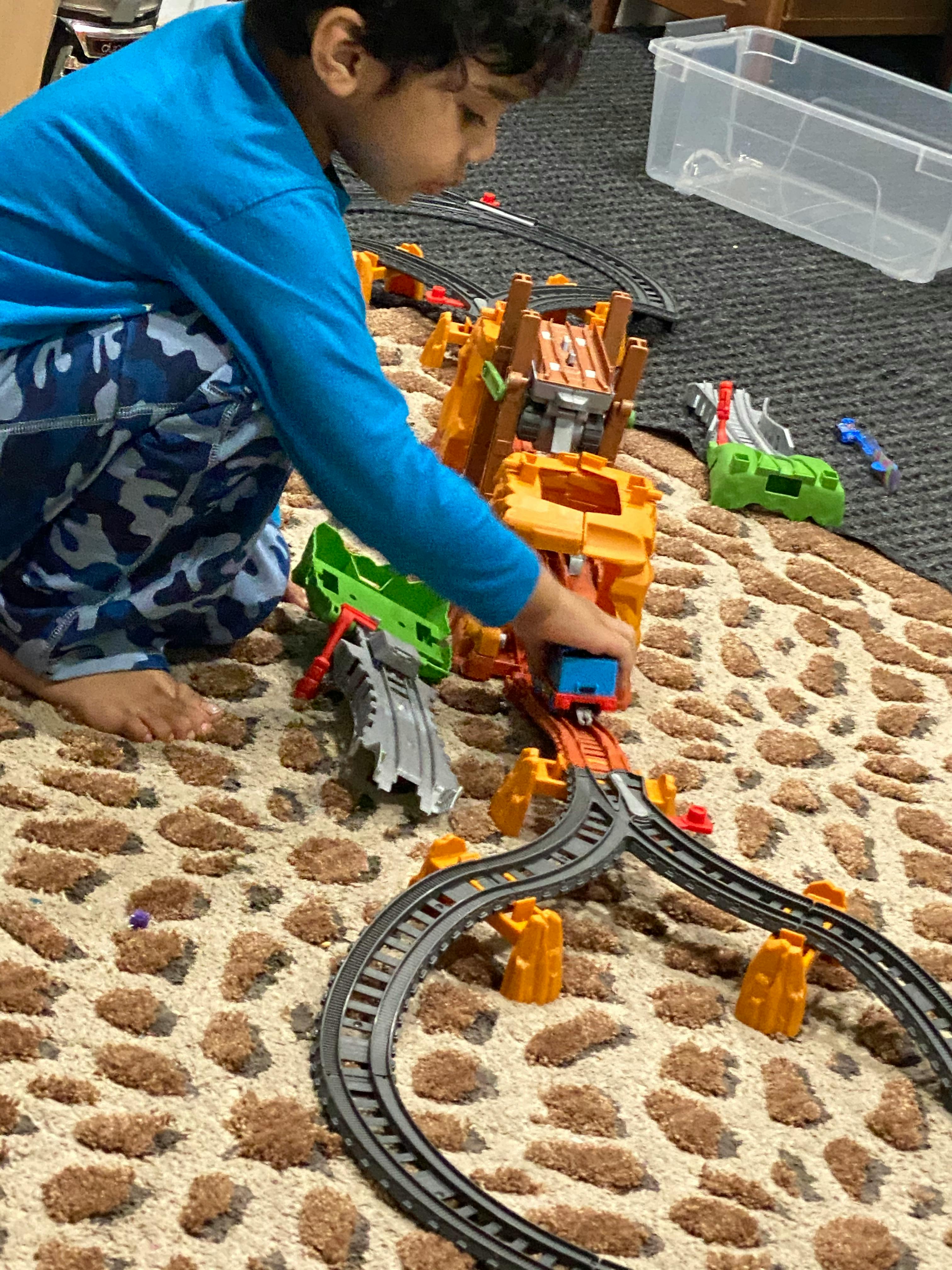 Child playing with a toy train set on a patterned rug