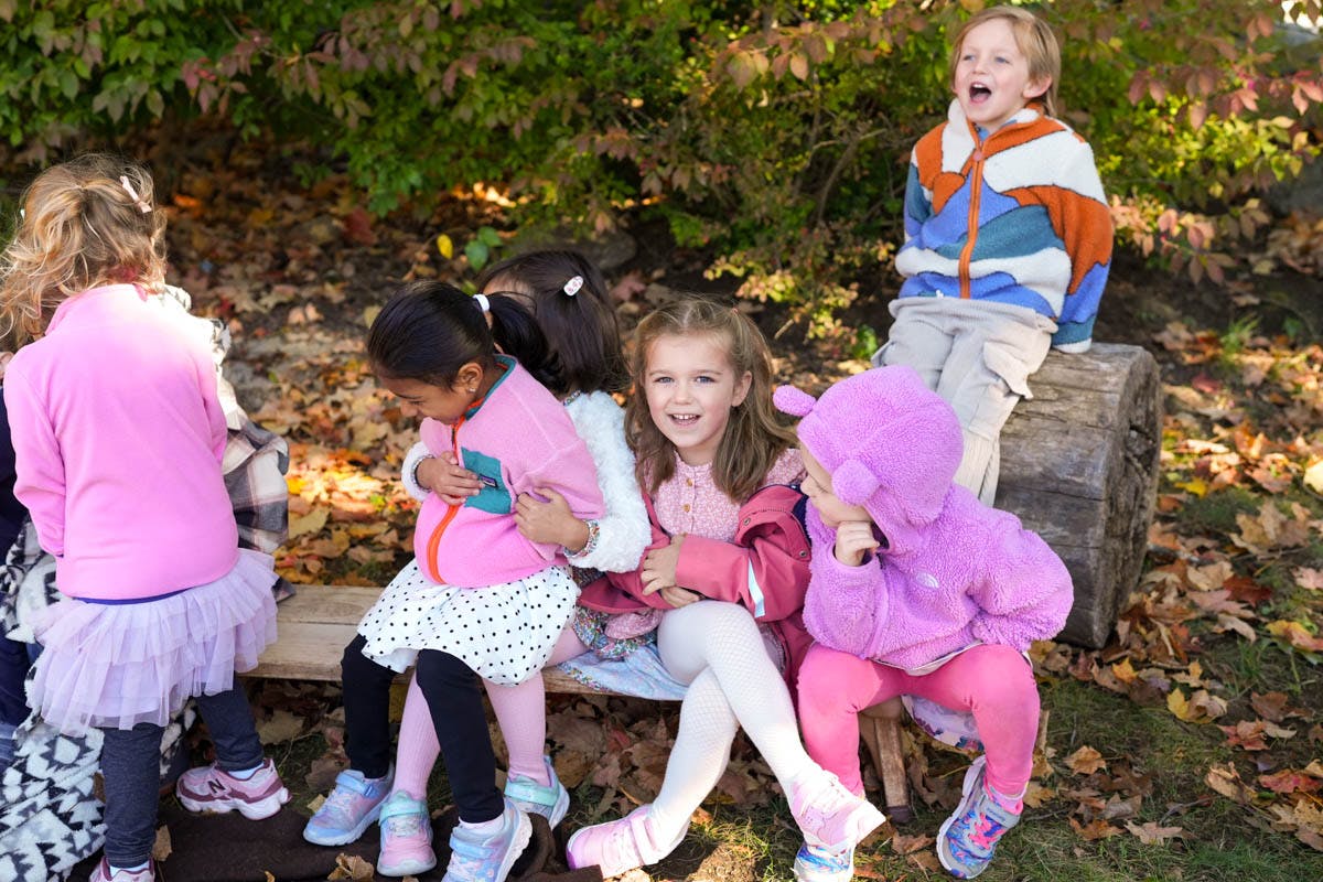 Children sitting outdoors, one child on a log and others on a bench