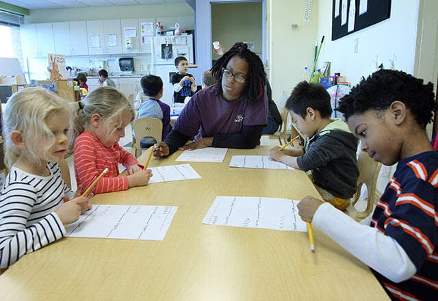 Adult and children writing at a table in a classroom