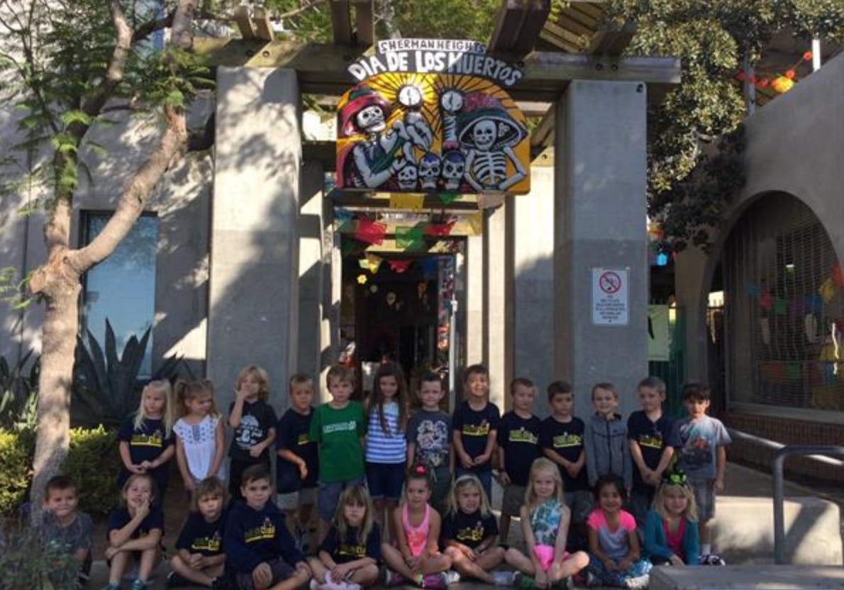 Group of children posing in front of a building with a "Dia de los Muertos" sign