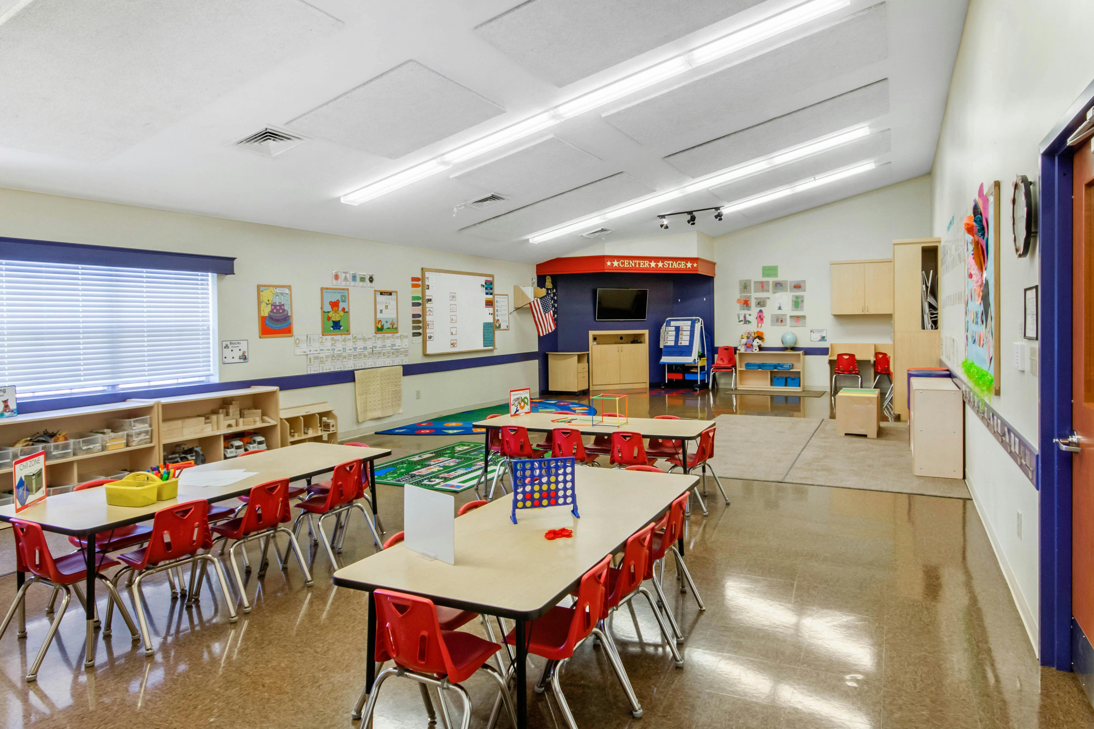 Classroom with multiple tables and red chairs, educational decorations on walls