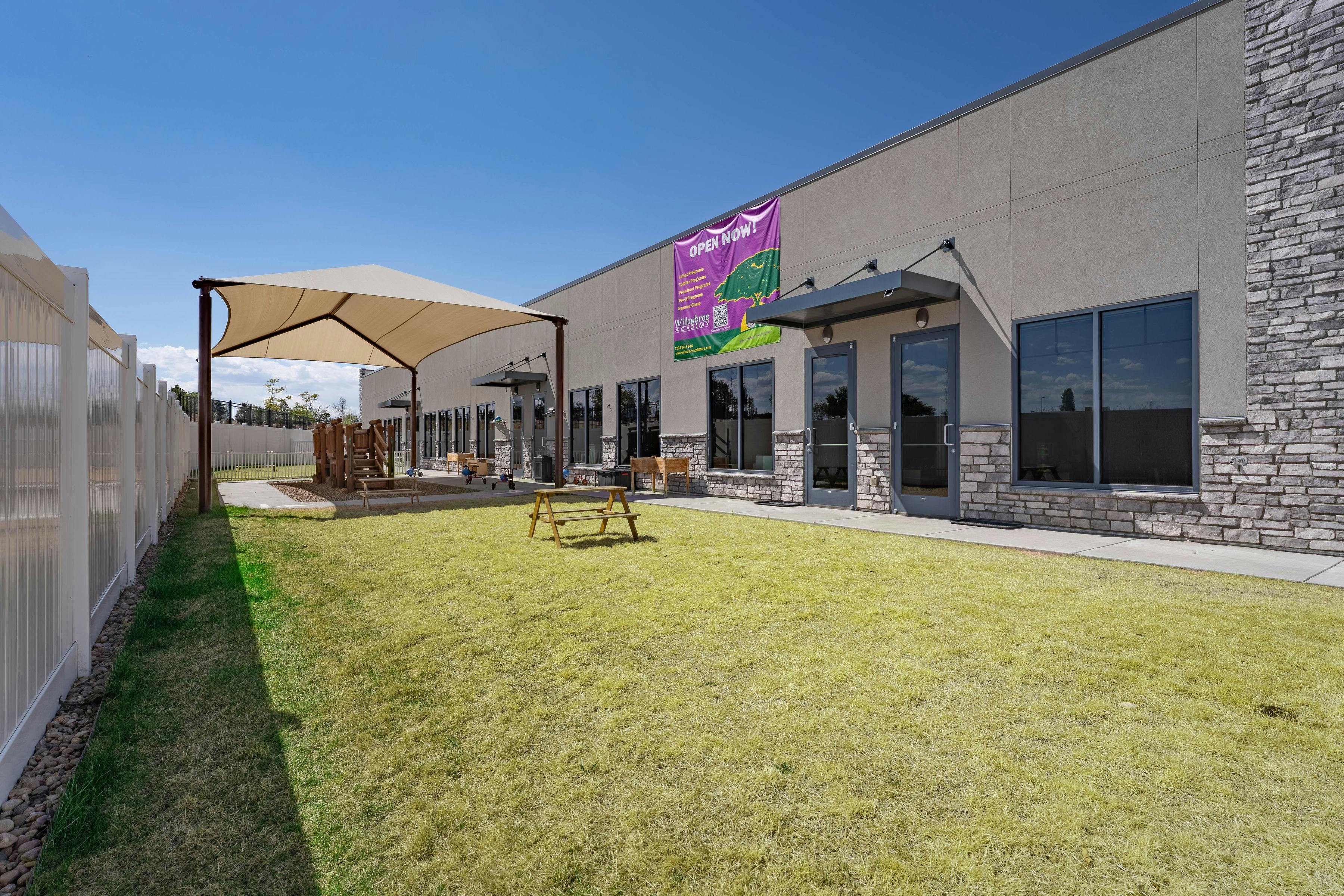 Child care center building with a "Open Now" banner, fenced outdoor play area