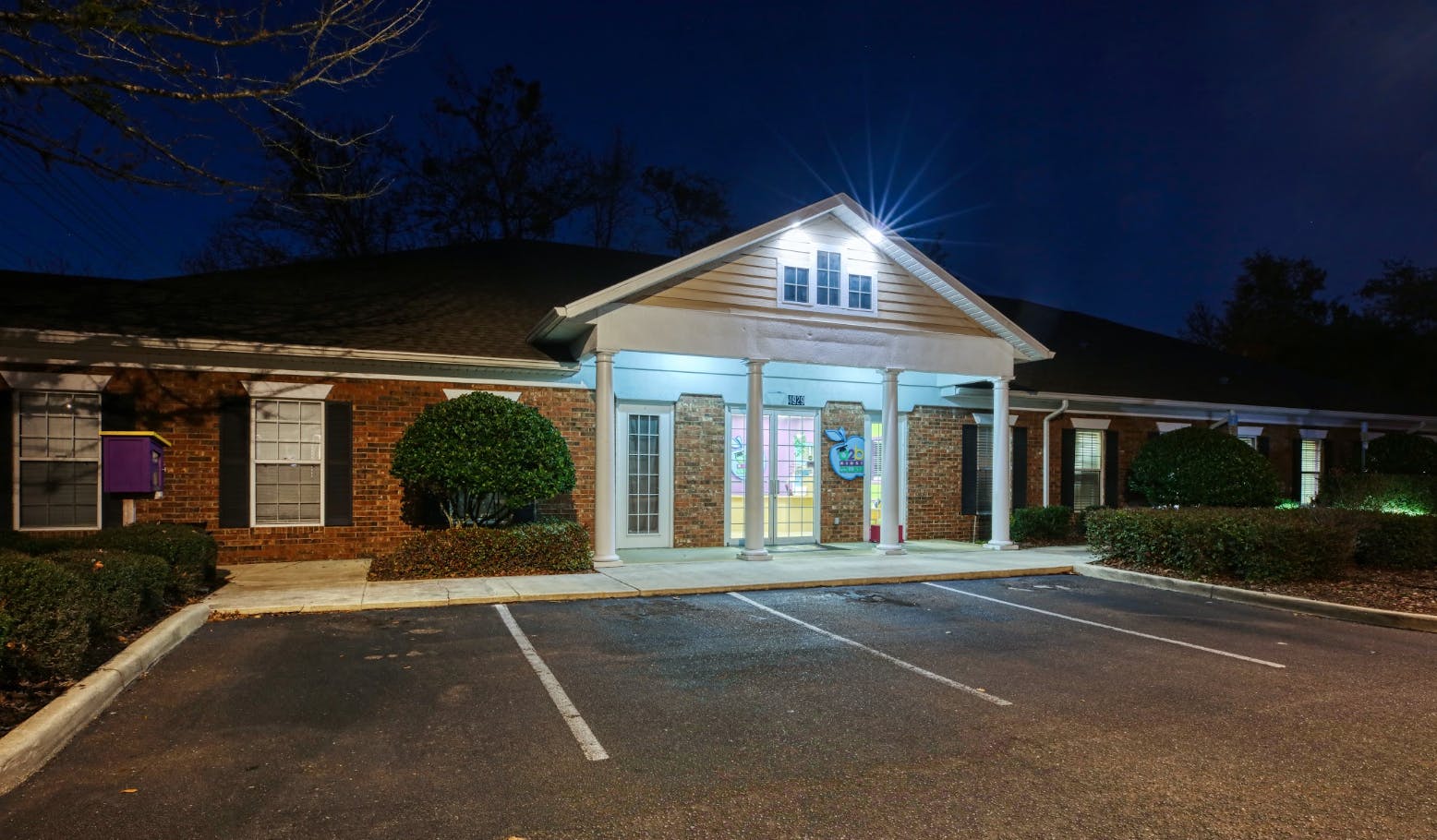 Brick building at night with a brightly lit entrance, a parking lot in the foreground