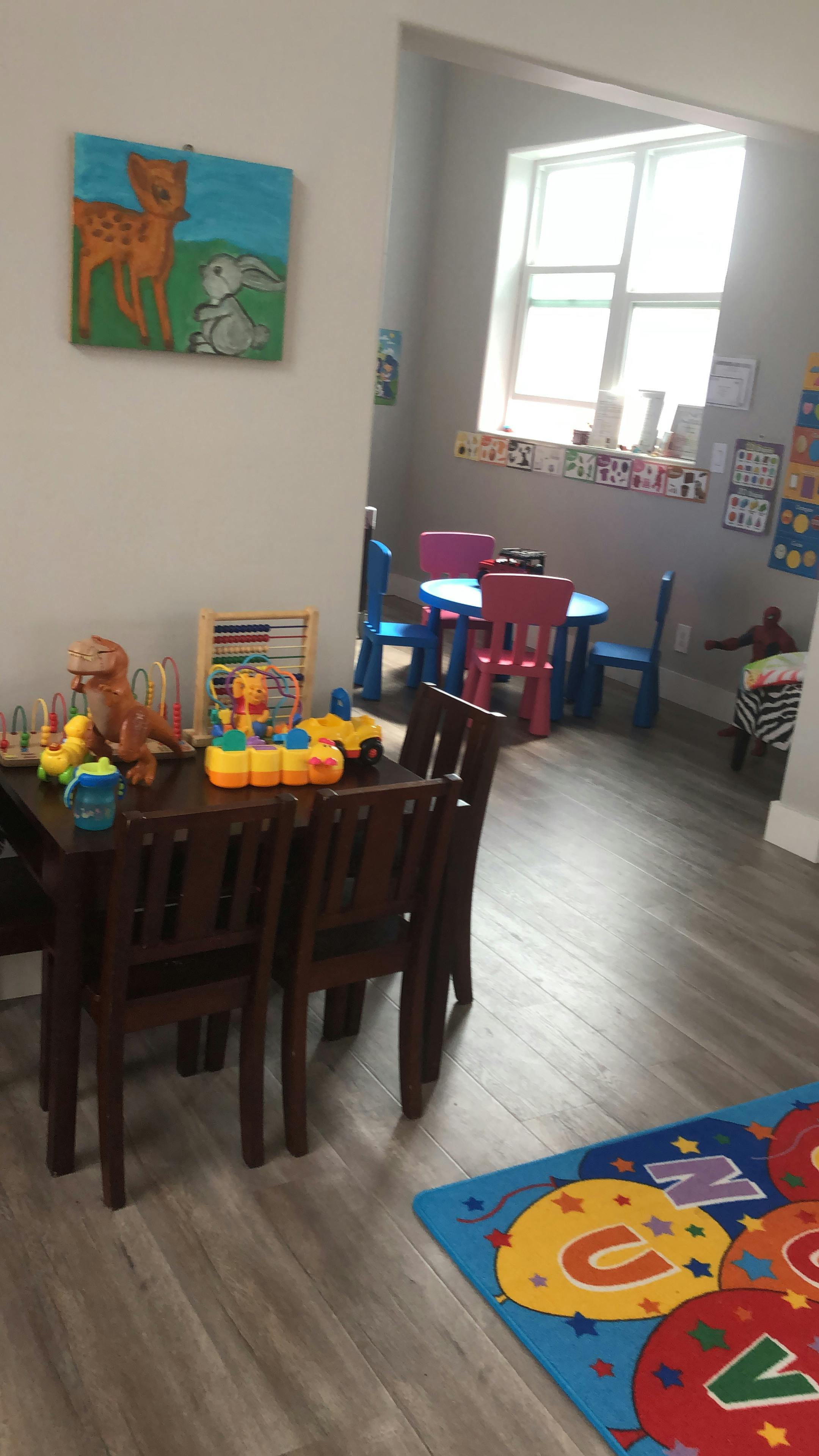 Playroom with small tables and chairs, toys on a table, and a colorful rug