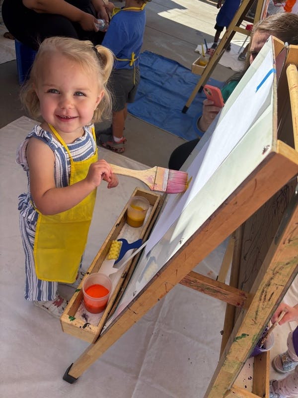 Child in a yellow apron painting on an easel