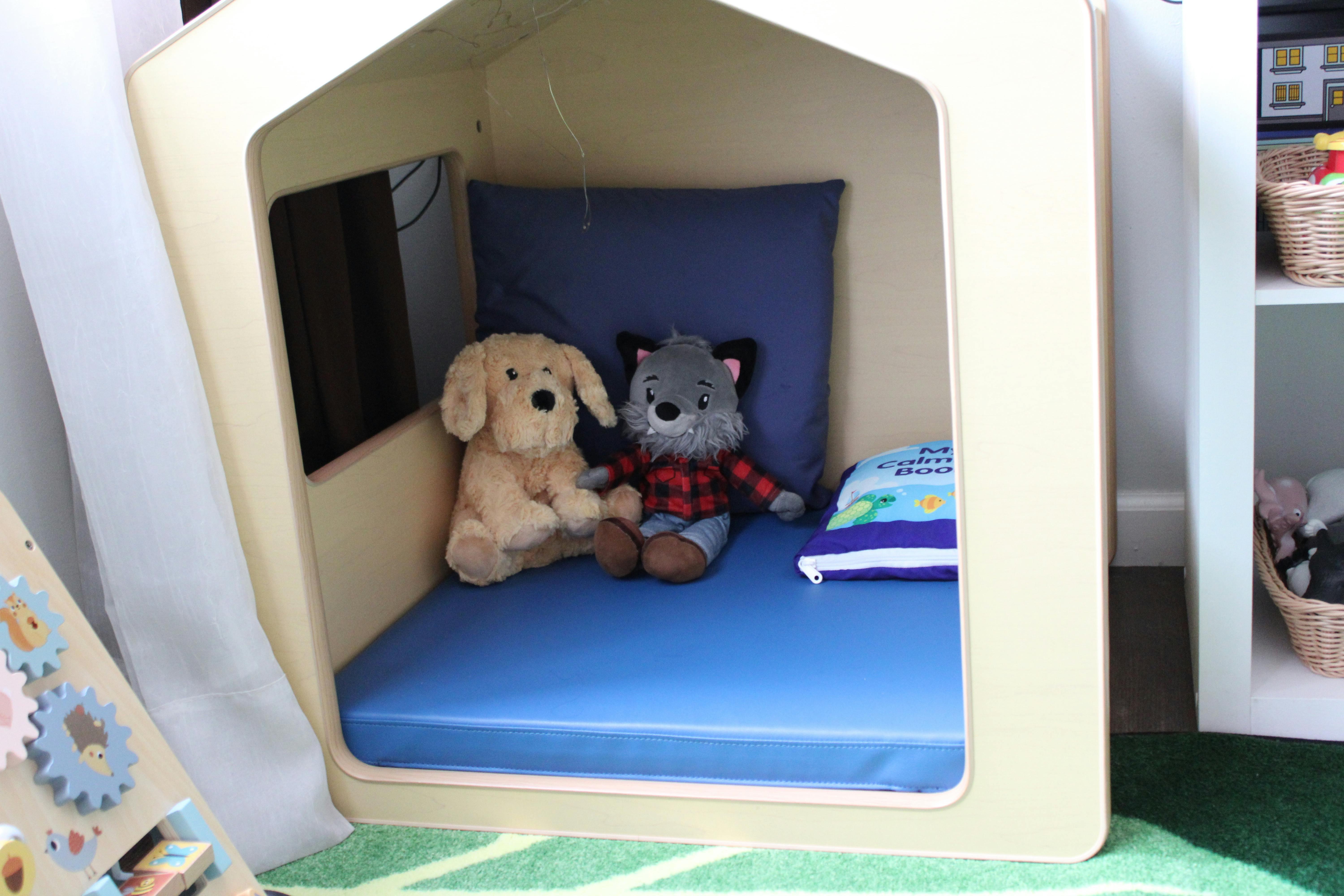 Stuffed dog and wolf in a small wooden playhouse with a blue cushion