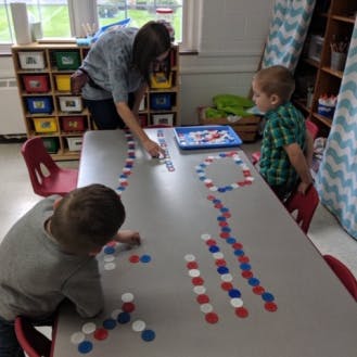 Adult and two children playing with colorful tokens at a table