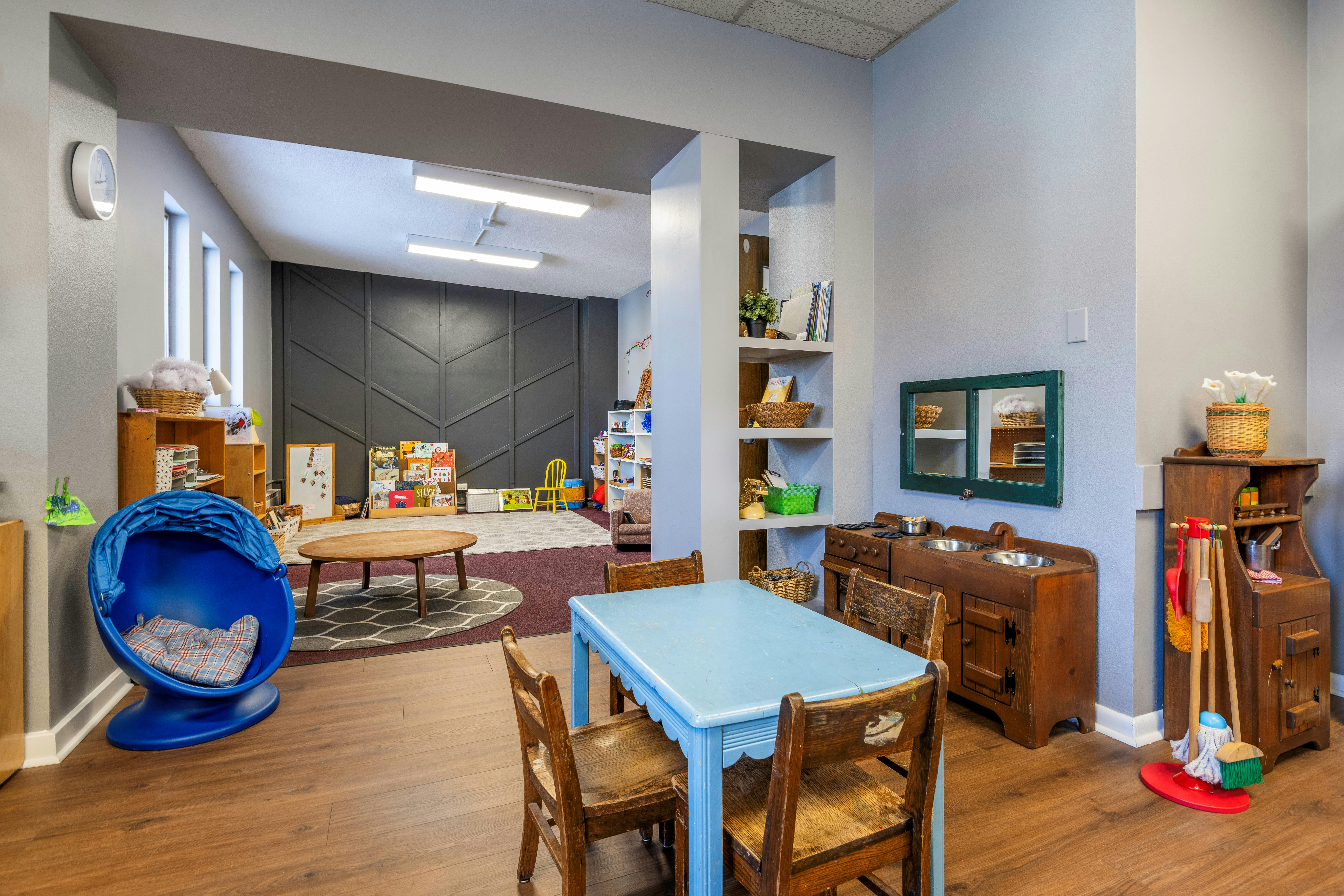 Children's play area with a blue table and chairs, toy kitchen, and reading nook