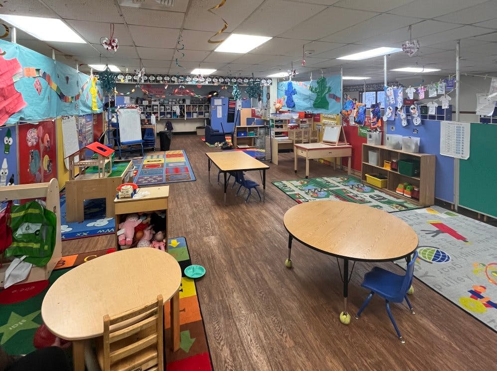 Empty colorful preschool classroom with tables, chairs, and play areas