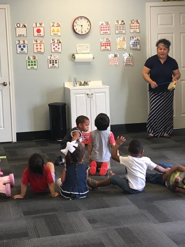 Adult standing in a classroom with several children sitting on the floor