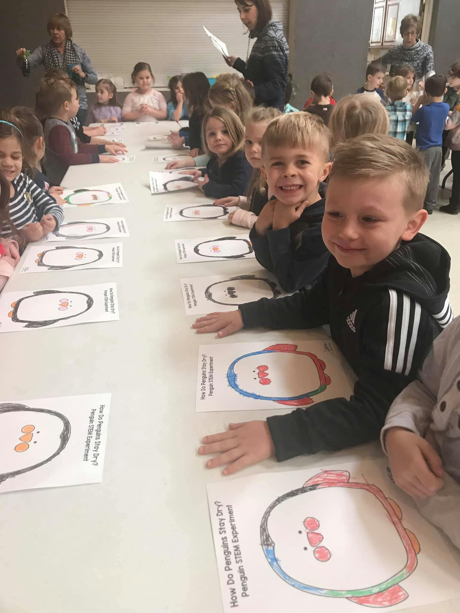 Children sitting at a table with penguin drawings