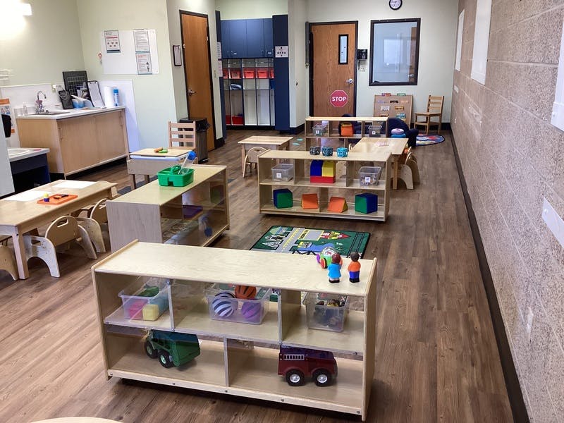 Classroom with child-sized tables, chairs, shelving units with toys
