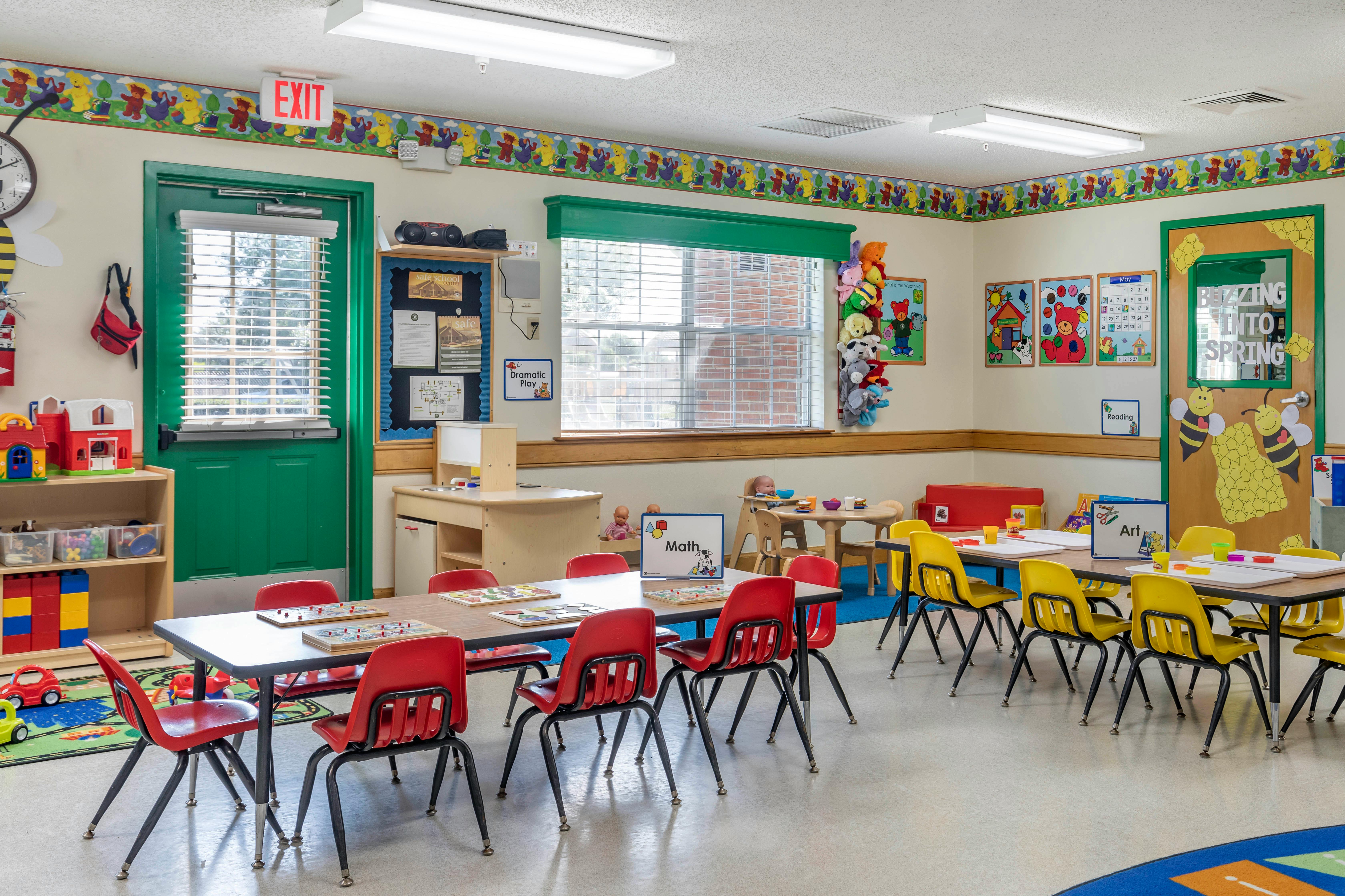 Empty children's classroom with small tables and chairs, toys, and learning posters